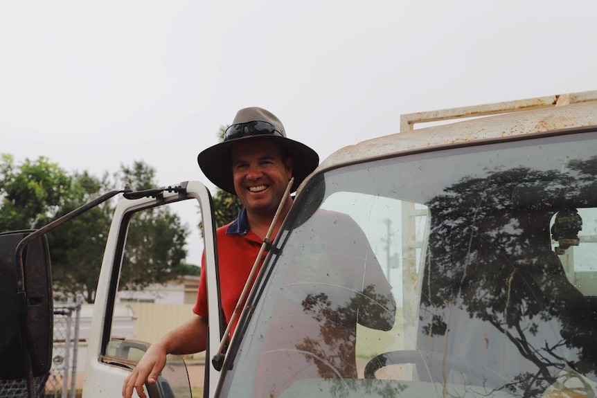 A man wearing a hat and leaning out the door of a truck and smiling.