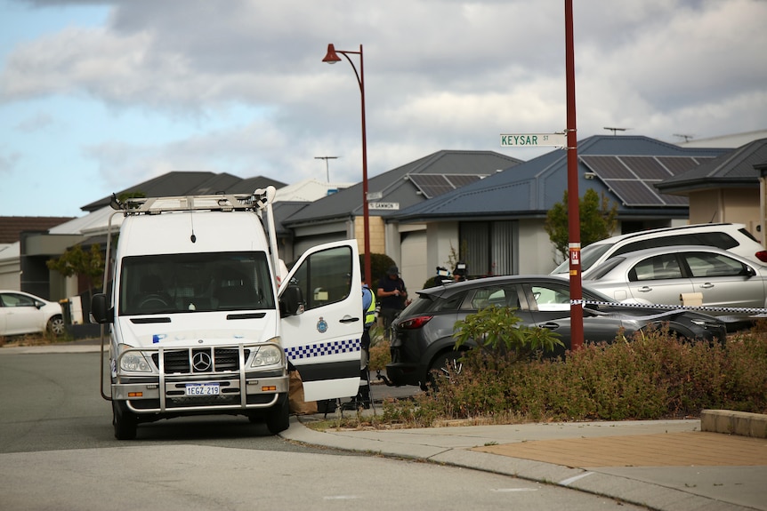 A wide shot of a police van, police officers and other vehicles on a suburban street.