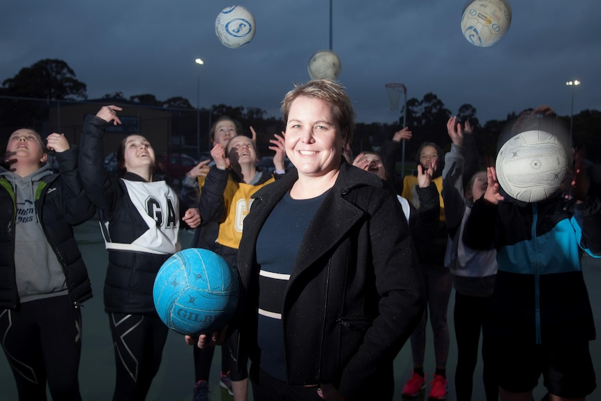 A woman holding a netball with young people in the background.