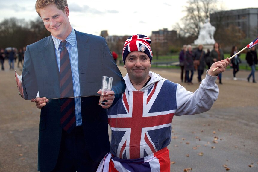 Royal watcher John Loughery dressed in clothes resembling the British flag poses with a cardboard cut out of Prince Harry