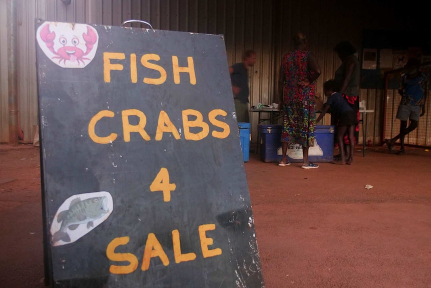 People are buying fish from a market, and there's a sign out the front.