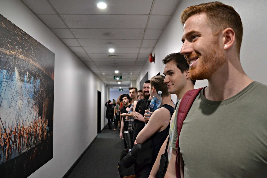 Men line up in a hallway before dance auditions.