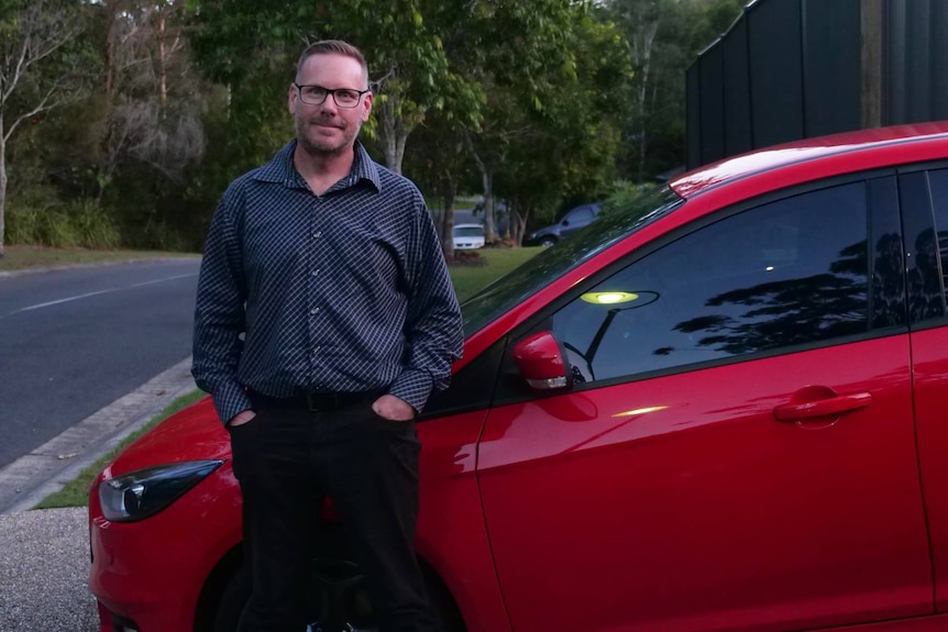 A man in smart casual clothes leaning on a red car