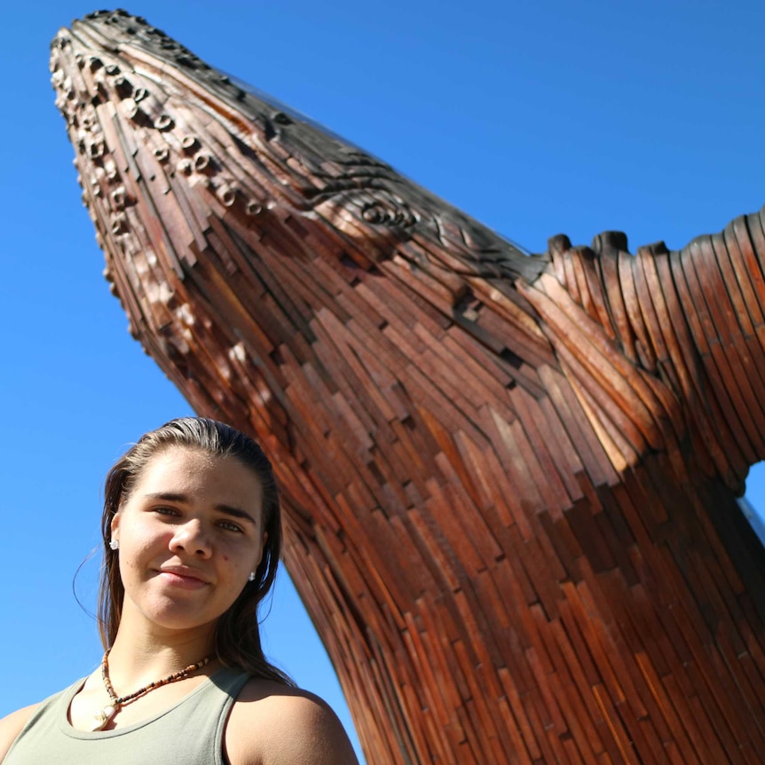A happy Yindi Clarke stands in front of a whale sculpture after graduating from Transition 2 Success in Hervey Bay.