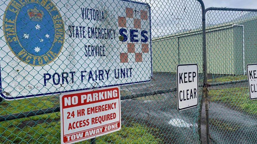 A padlocked gate in front of large sheds, with an SES sign on the fence.