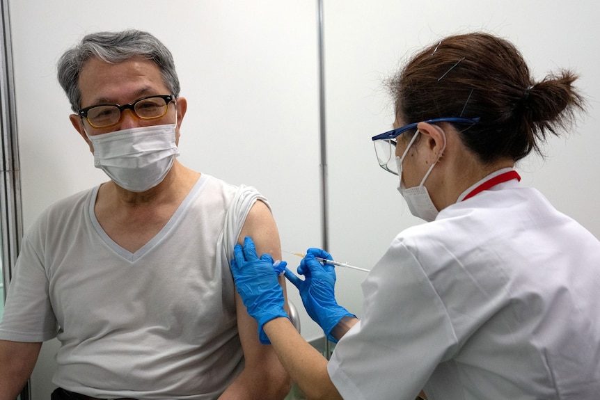 A male pensioner receives the Moderna COVID-19 vaccine from a female nurse at a mass vaccination centre in Tokyo