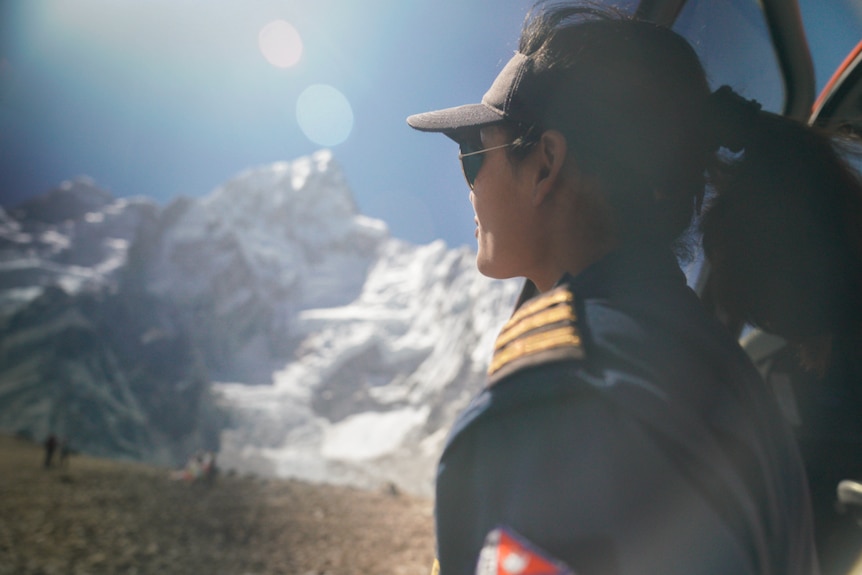 A woman in a pilot uniform looks out at a snowy peak from a chopper