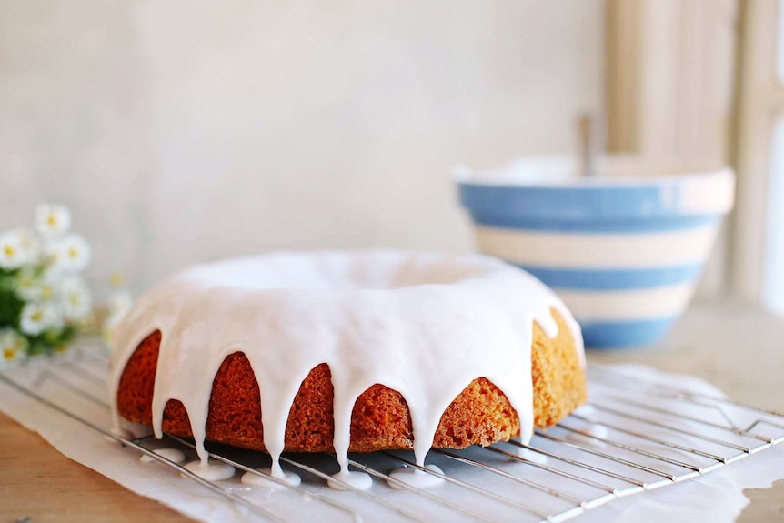 A bundt cake with fresh icing sits on top of a baking rack with a mixing bowl in the background.