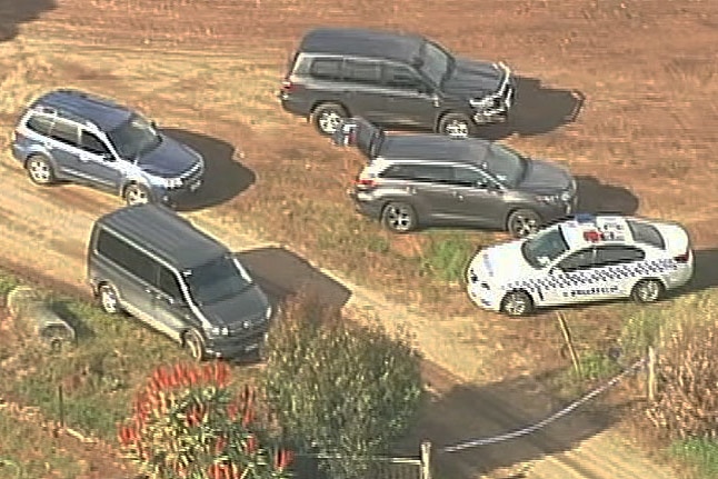 Five cars including a police car parked on a dirt road near the farmhouse.