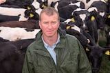 A man in a green wet weather jacket stands in front of a herd of black and white cows.
