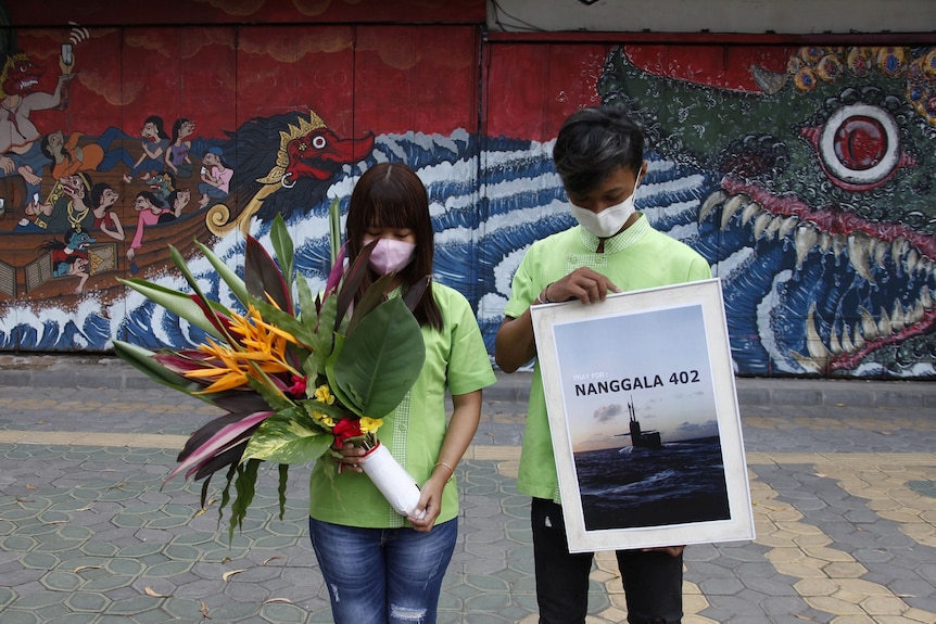 People holding a placard and flowers bow as they pray for the crew of submarine KRI Nanggala-402.