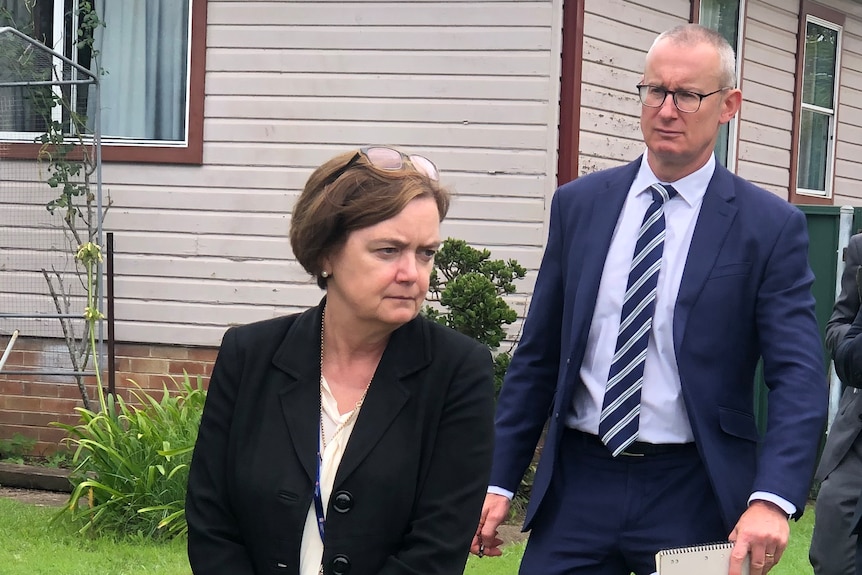 A group of lawyers and police where suits walk outside a house in a country town.