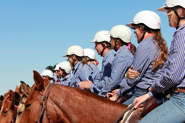 A line of young people on horses with white helmets on.