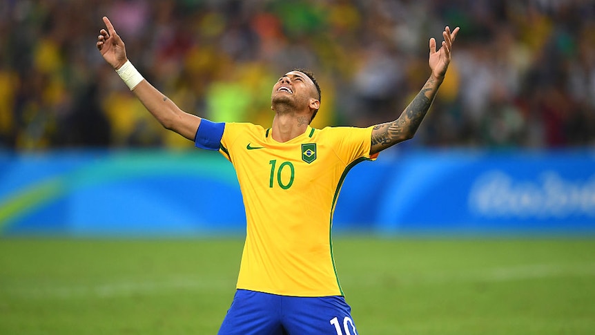 Brazilian soccer player Neymar kneels on the ground with hands raised in celebration of scoring the winning penalty.