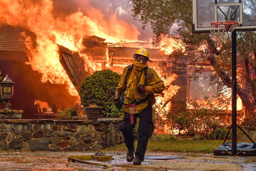 A fireman walks away from buildings that are engulfed in flames.