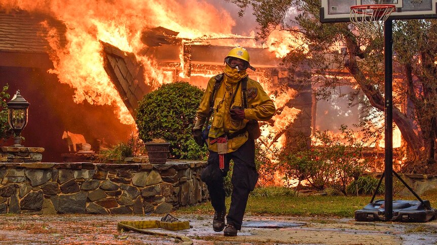 A fireman walks away from buildings that are engulfed in flames.