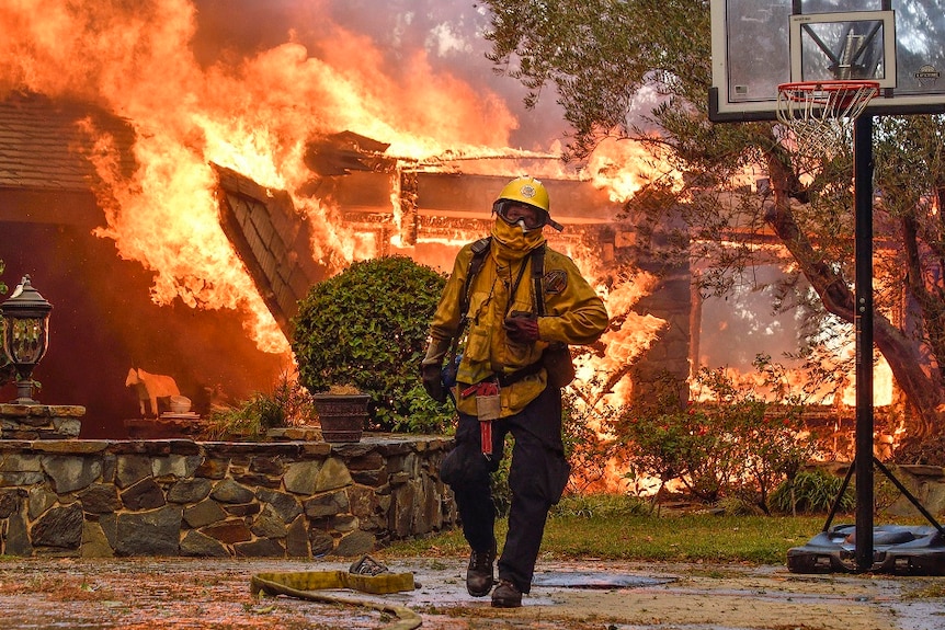 A fireman walks away from buildings that are engulfed in flames.