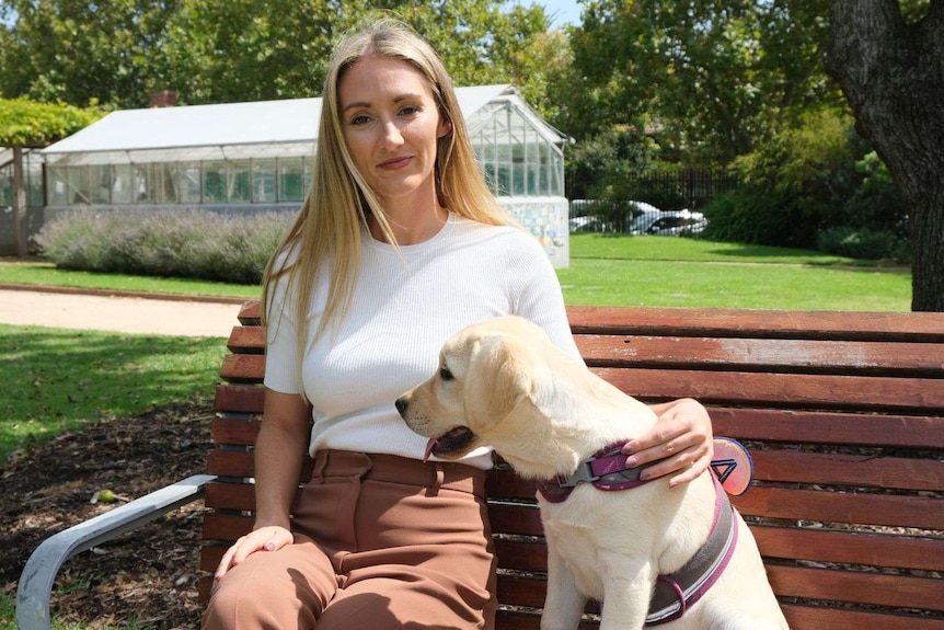 Keely Walsh sits holding Labrador puppy Luna on a park bench