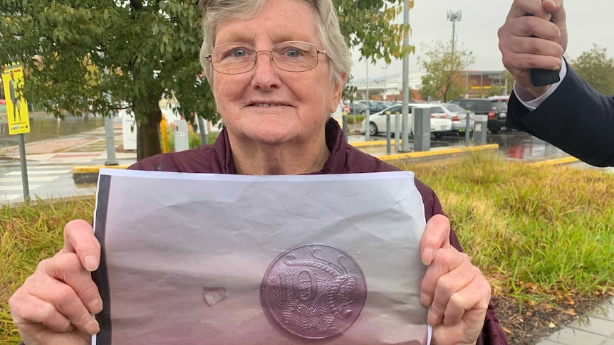 Patricia Smith holds a piece of paper showing a piece of glass next to a 10 cent coin.