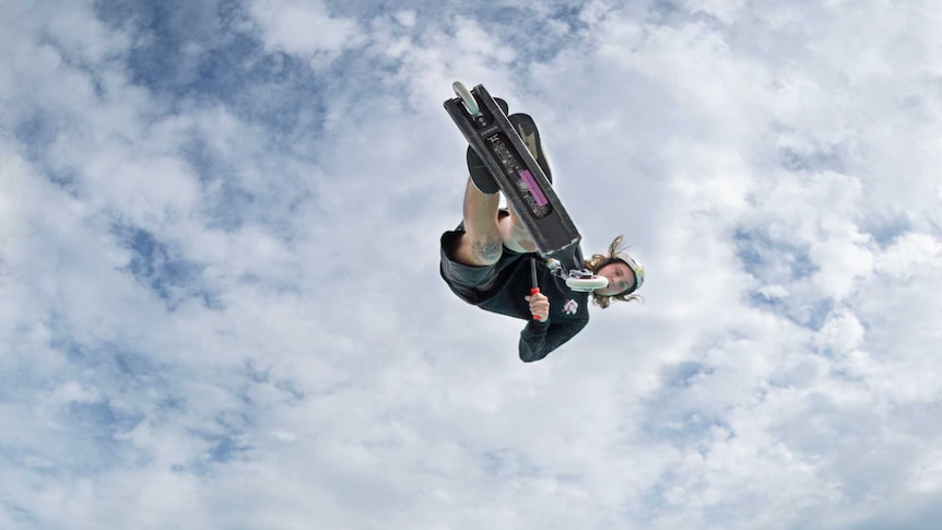 A young man on a scooter floating high above a deep skate bowl