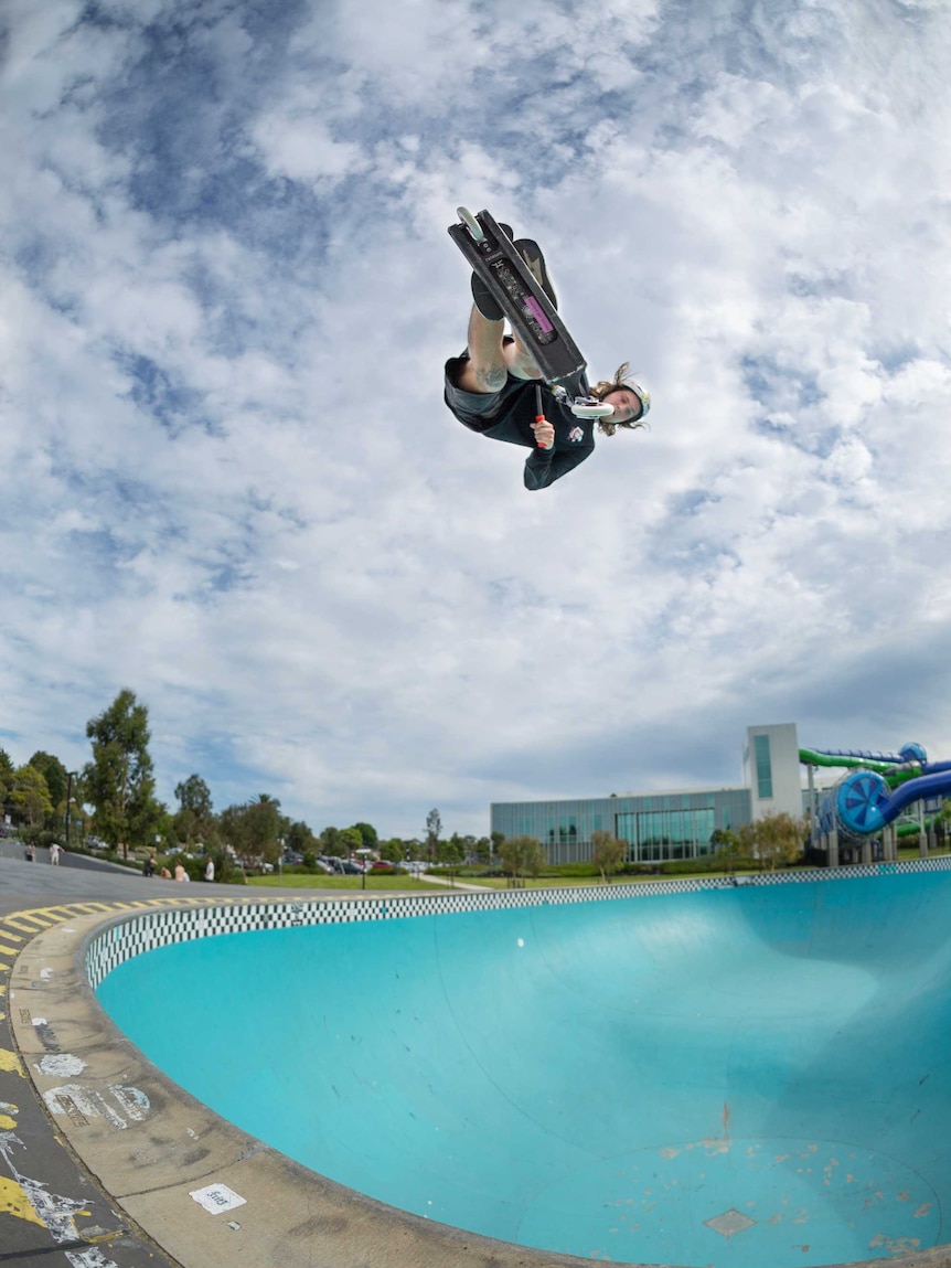 A young man on a scooter floating high above a deep skate bowl