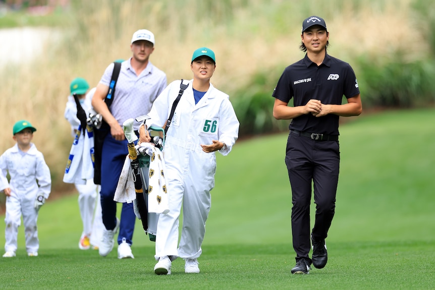 Crowd in background watching a golf tournament. A male golfer in black has hands up in the air next to his female caddy, smiling