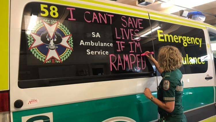A paramedic writes the words 'I can't save lives if I'm ramped' on an ambulance in pink