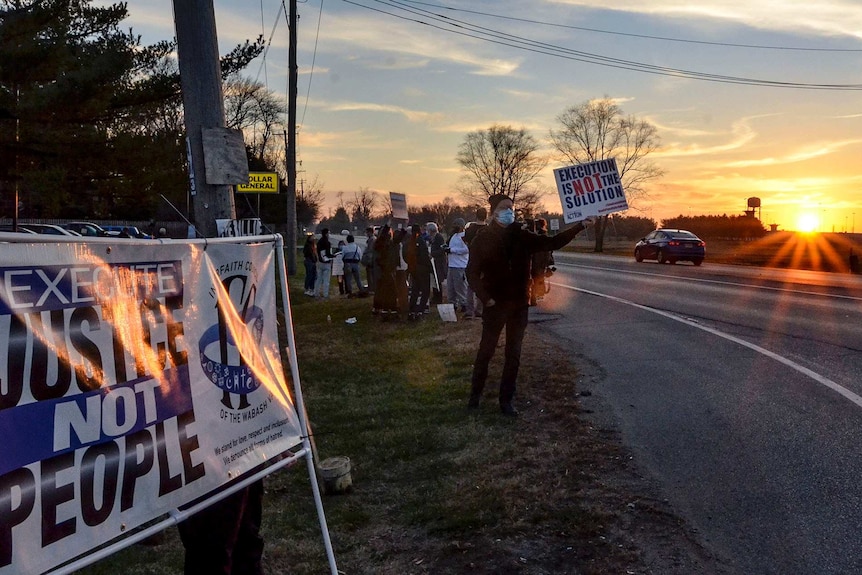 Protesters hold up placards on a road as a car drives past while the sun sets