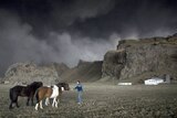 A farmer tries to lure his horses back to the stable as a cloud of black ash looms overhead.