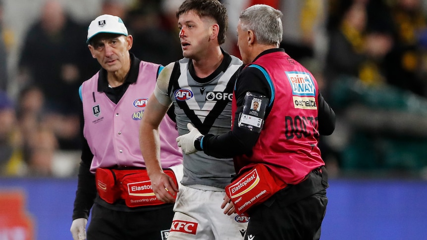A man is escorted off an AFL field after a heavy head clash 