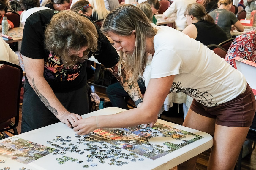 A man and a woman stand at a table and piece together a puzzle under competition 