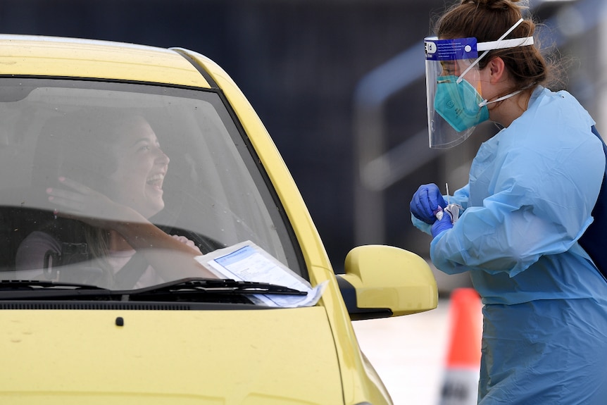 A woman in a car smiles at a woman wearing a face shield and face mask