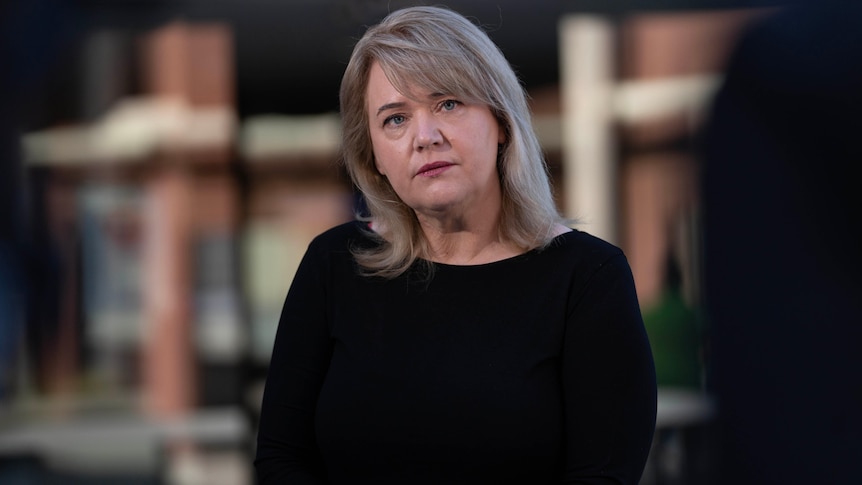 A woman with blonde hair stands in front of a building