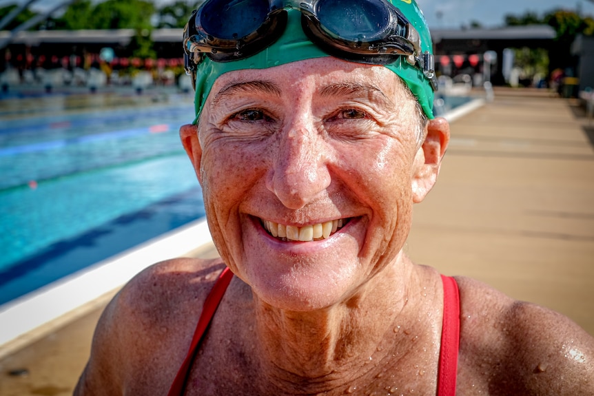 Closeup headshot of woman wearing swim goggles and hat at a pool.