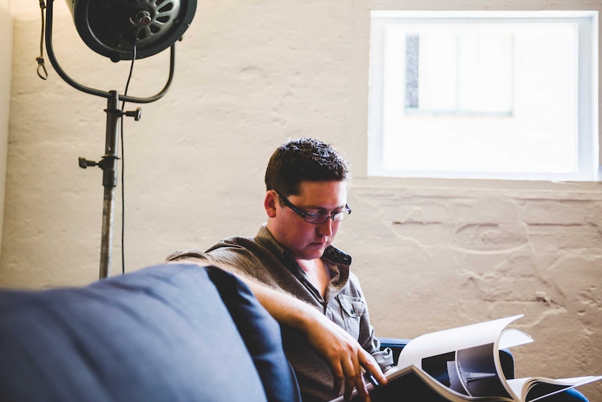 Patrick Clair sits on a couch perusing a book