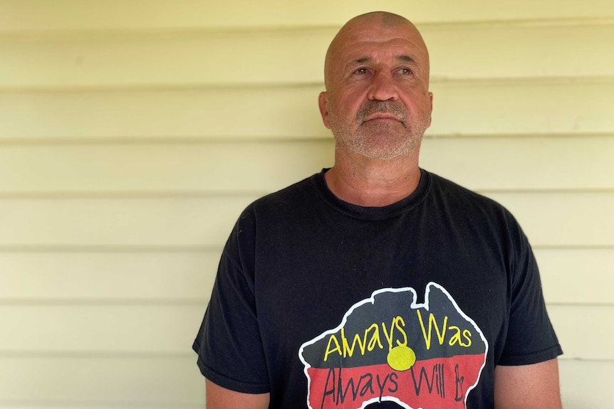 A man wears a t-shirt with the Aboriginal flag in the shape of Australia on it, with the words 'Always Was, Always Will Be'.