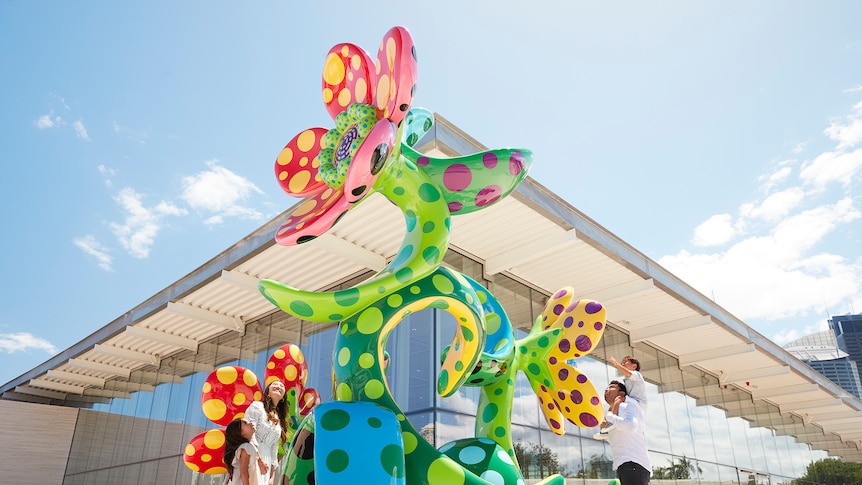 A large, multi-coloured and dotted sculpture of flowers, standing outside a building of panelled windows