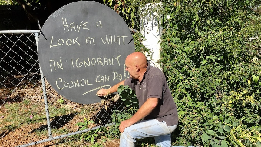 Man writes a message on a blackboard which is located on the kerbside