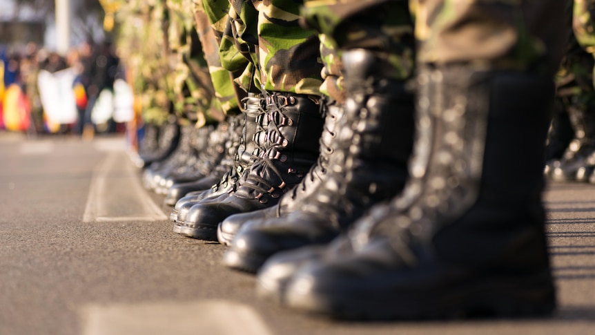 A line of army boots worn by soldiers in khaki uniforms