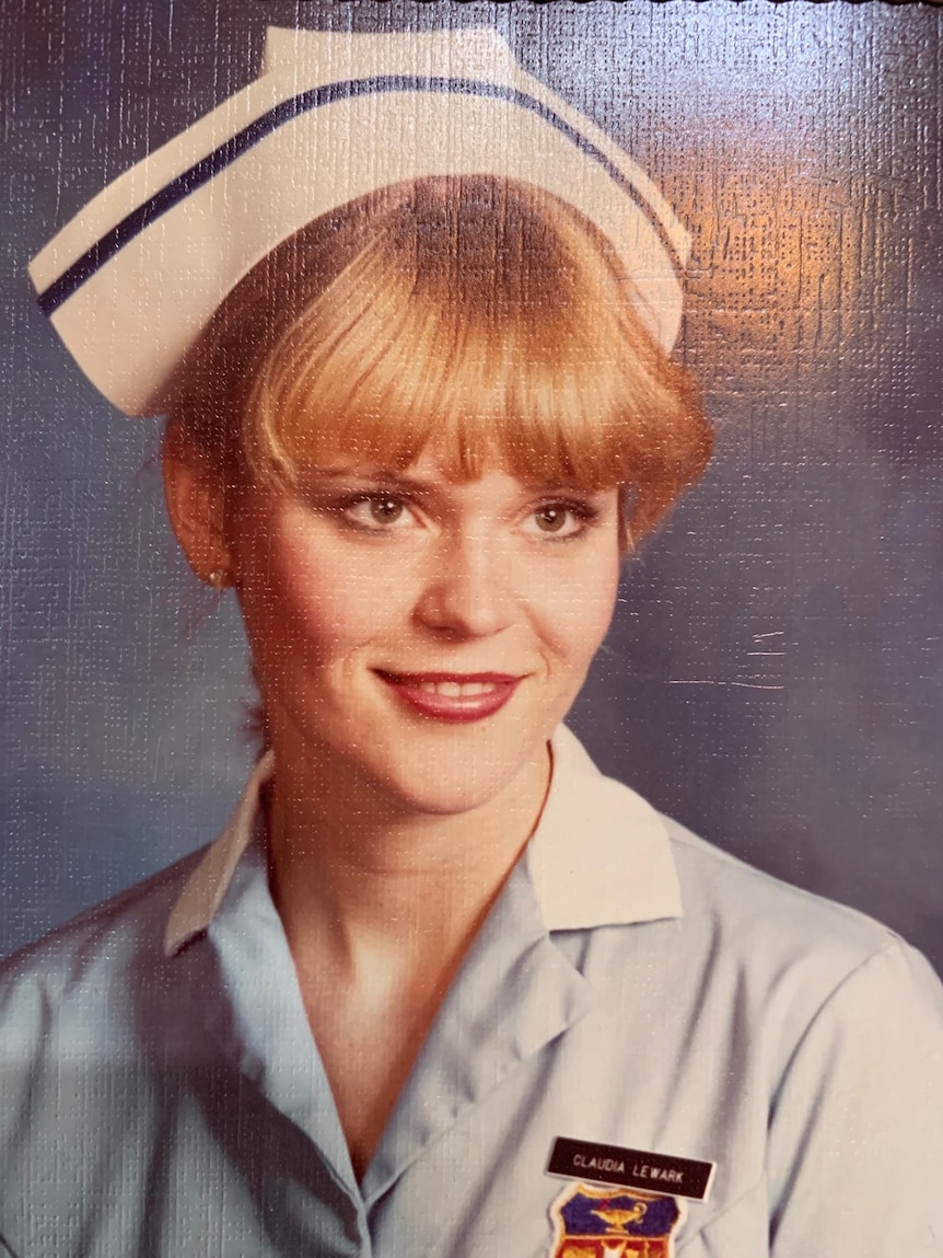 A young woman in a nurse's uniform smiles.