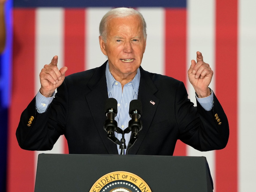 Joe Biden stands at a lectern with his hands in the air 