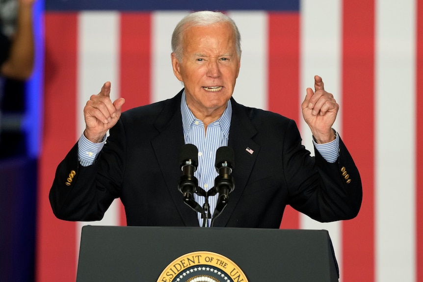 Joe Biden stands at a lectern with his hands in the air 