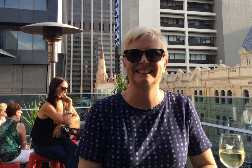 A woman smiles while sitting on a rooftop bar with the Perth skyline in the background.