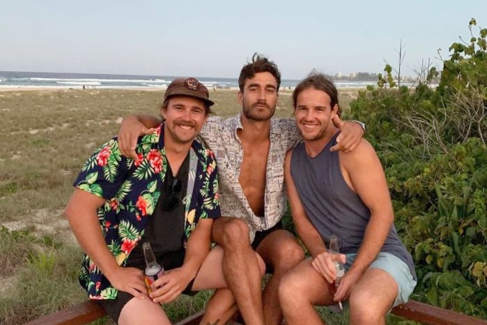 Three men sit in front of a beach for a story on working as a plumber in Antarctica