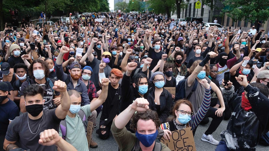Thousands of protesters kneel on a long street and raise fists as part of a wide series of demonstrations across the US.
