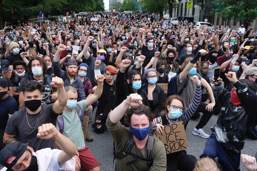 Thousands of protesters kneel on a long street and raise fists as part of a wide series of demonstrations across the US.