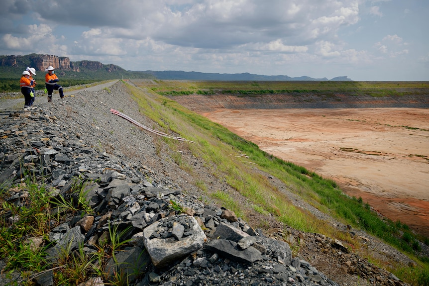 a mine wall with two people in hi-vis clothing standing on top.