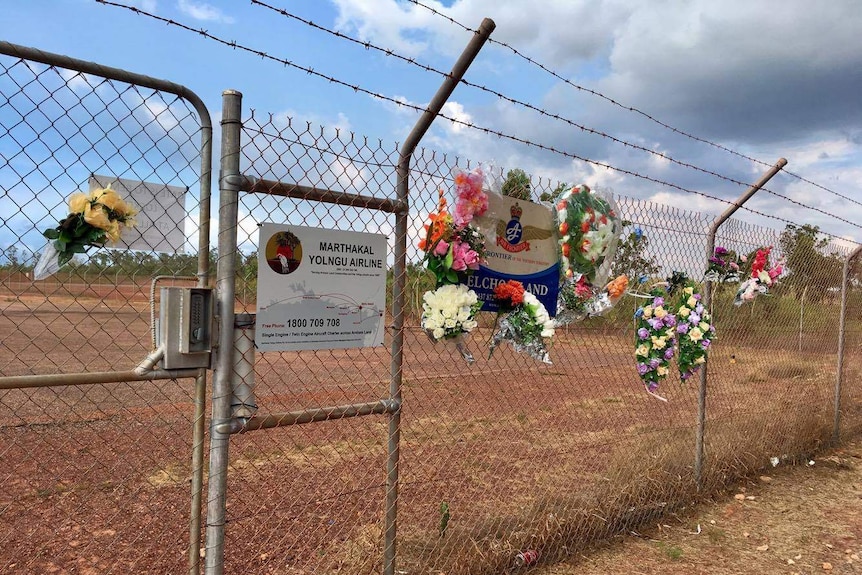Around twelve bunches of flowers attached to airport fence.