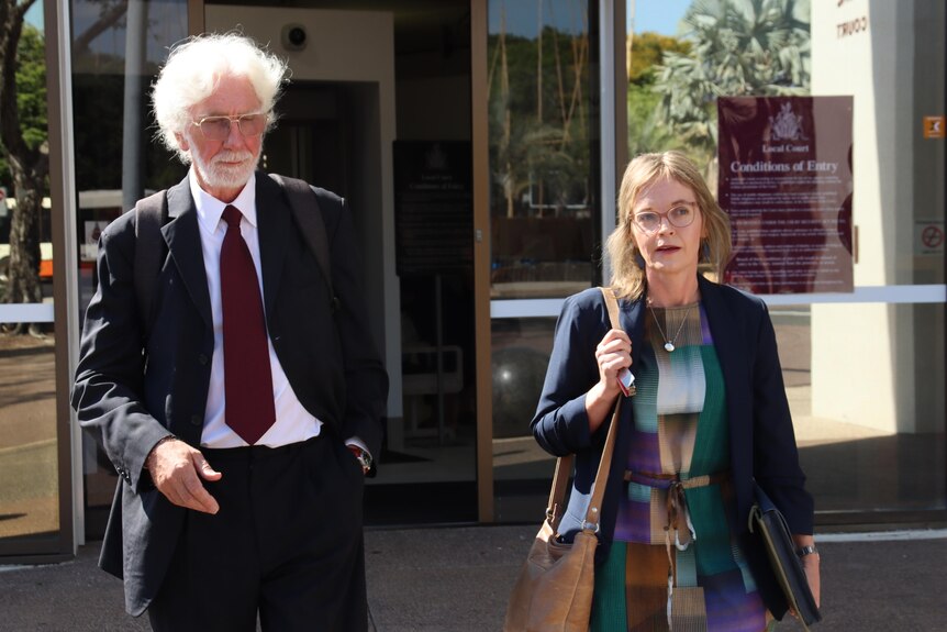 An man with a white beard and a woman in a multi-coloured dress walk out of the Darwin Local Court