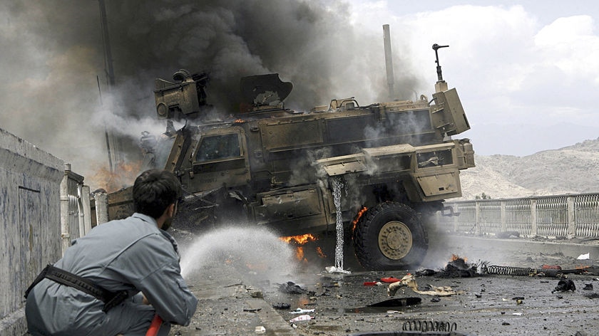 An Afghan policeman tries to put out fire from a burning US armoured vehicle.